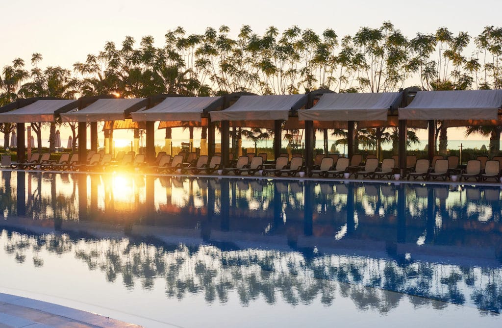 Ein Swimmingpool mit Liegestühlen und Sonnenschirmen bei Sonnenuntergang im Luxushotels Belek.