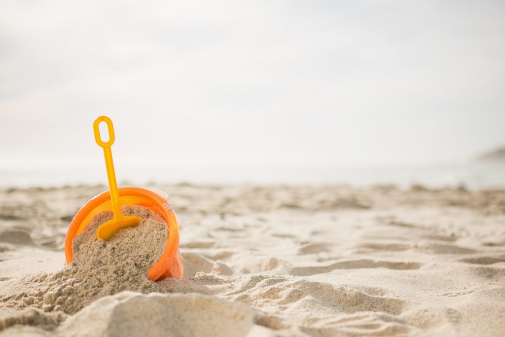 Ein orangefarbener Eimer, der auf dem Sand am Strand in der Türkei sitzt.