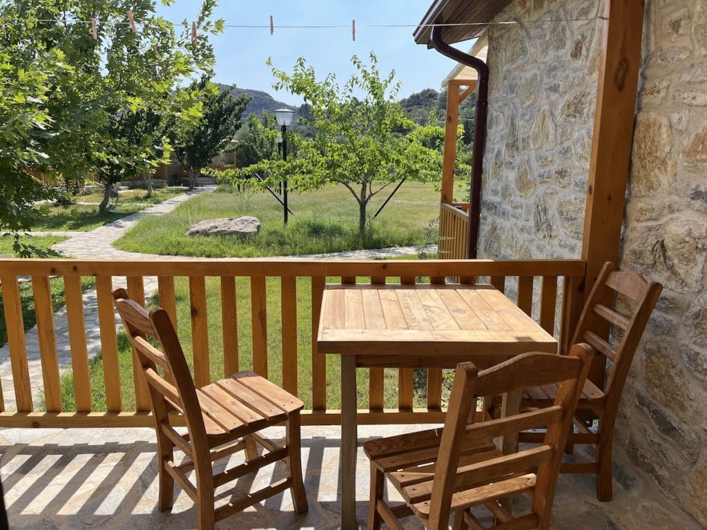 Holztisch und Stühle auf einer Datca-Veranda mit Blick auf einen sonnigen Garten mit Bäumen.