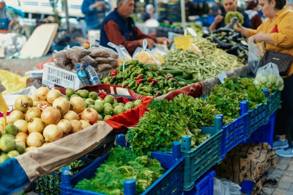 Kunden und ein Verkäufer auf einem lebhaften Outdoor-Markt in Datca mit frischem Obst und Gemüse.