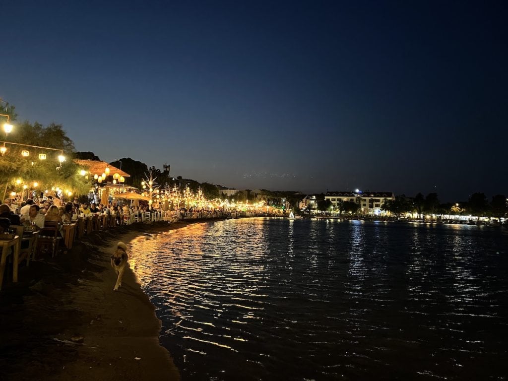 Abends an einer belebten Strandpromenade in Datca mit Lichtern, die sich im Wasser spiegeln.