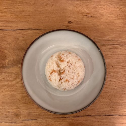 Ein Teller mit einer kleinen Portion Reis auf einem Holztisch.
