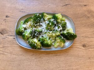 Ein rechteckiger Teller mit Brokkolisalat, garniert mit geriebenem Parmesankäse, auf einem Holztisch.