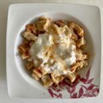 Ein Teller mit Manti, garniert mit Knoblauchjoghurt und Butter, serviert auf einem weißen Teller mit rotem Blumenmuster.