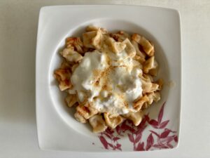 Ein Teller mit Manti, garniert mit Knoblauchjoghurt und Butter, serviert auf einem weißen Teller mit rotem Blumenmuster.