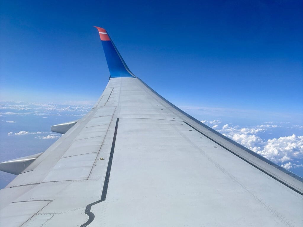 Blick auf einen Flugzeugflügel vor einem Hintergrund aus blauem Himmel und vereinzelten Wolken, aufgenommen aus der Perspektive eines Passagiers auf dem Flug in die Türkei