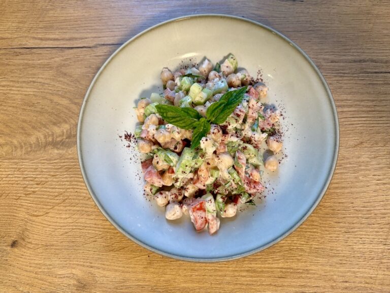 Eine Schüssel Nohut Salatası mit Gurkenwürfeln, Tomaten und Minzgarnitur steht auf einem Holztisch.