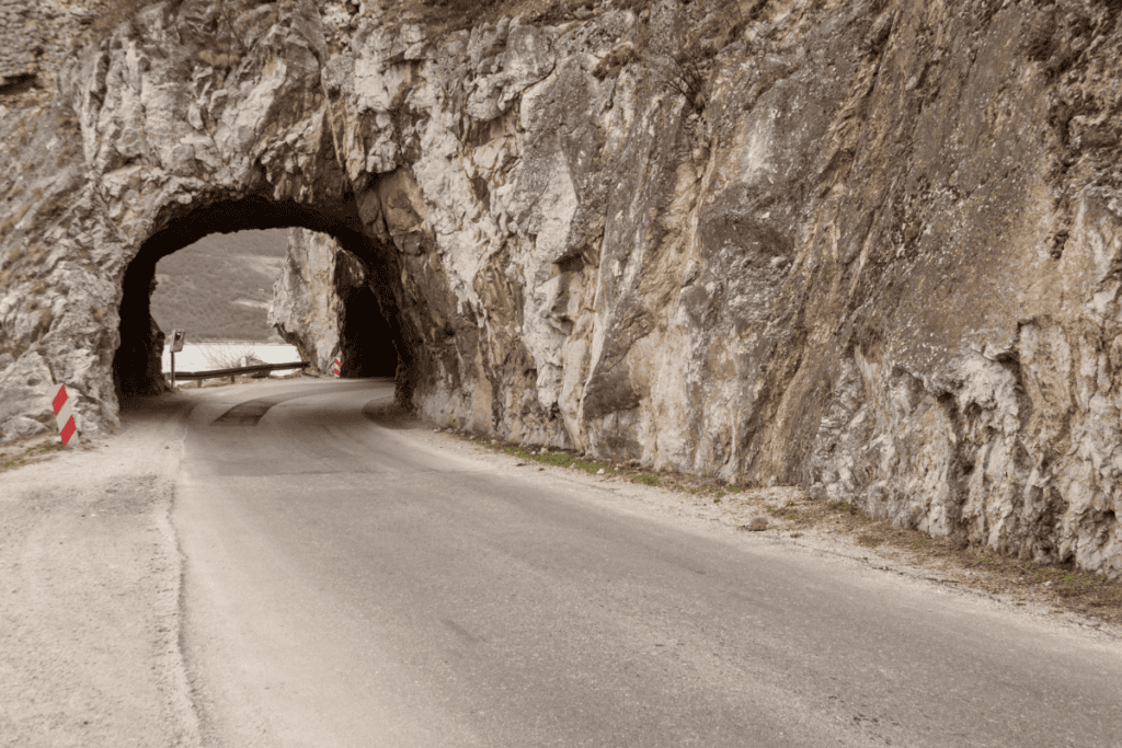 Eine schmale Straße in Serbien schlängelt sich durch einen Felstunnel mit Blick auf die dahinterliegende Landschaft.