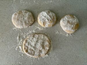 Vier leicht mit Mehl bestäubte Teigbällchen ruhen auf einer gesprenkelten Arbeitsplatte.