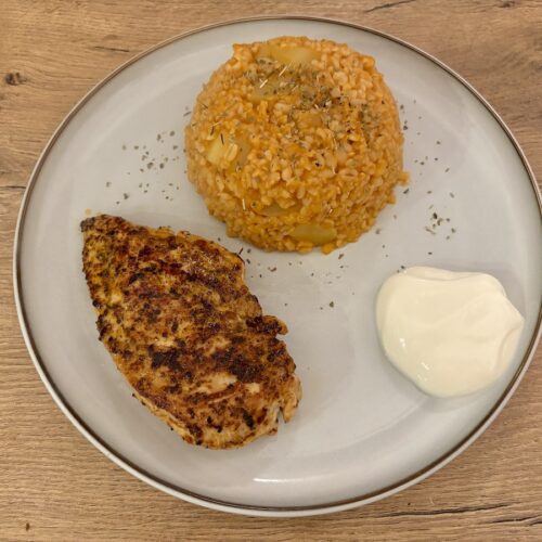 Gegrillte Hähnchenbrust, Bulgur Pilav mit Kartoffeln und einer Portion Joghurt auf einem Teller.