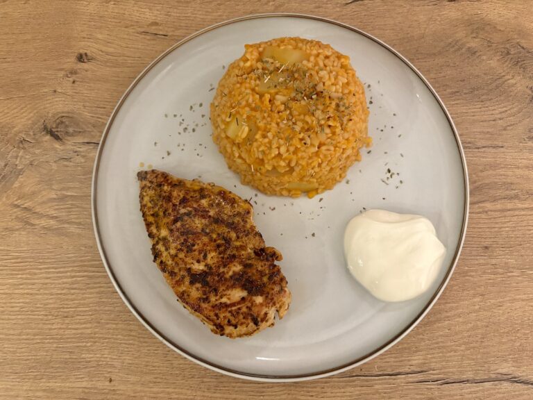 Gegrillte Hähnchenbrust, Bulgur Pilav mit Kartoffeln und einer Portion Joghurt auf einem Teller auf einer Holzfläche.