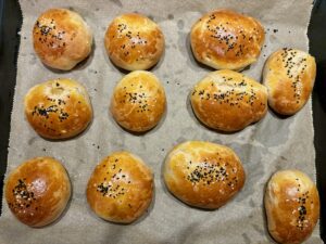 Fertig gebackene Hefeteigbrötchen mit einer goldigen Oberfläche auf einem Backblech mit Backpapier bestreut mit Schwarzkümmel und Sesam