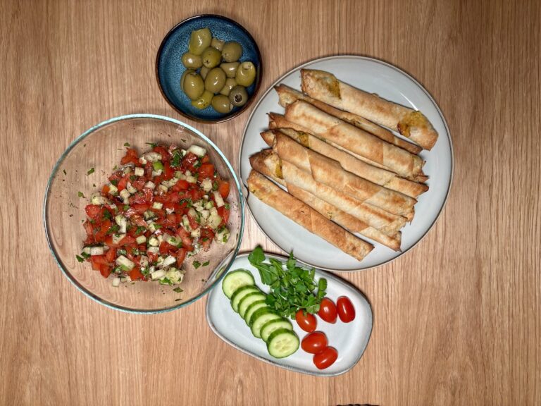 Auf Einem Tisch Stehen Ein Teller Mit Sigara Börek, Eine Schüssel Erfrischenden Gavurdağı Salatası Mit Tomaten Und Gurken, Eine Kleine Schüssel Oliven Und Eine Platte Mit Gurkenscheiben, Kirschtomaten Und Kräutern.