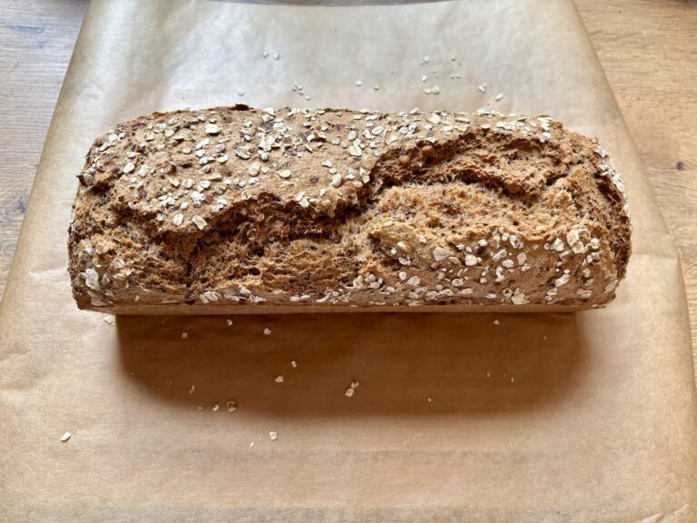 Ein rechteckiger laib dinkel vollkornbrot mit haferflocken liegt auf einem blatt braunem backpapier.