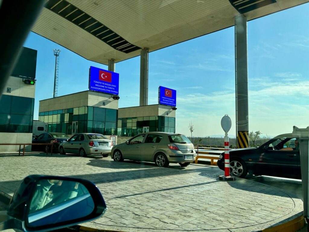 Autos warten in einer Schlange an einem Grenzkontrollpunkt in der Türkei. Auf elektronischen Schildern über den Kabinen sind türkische Flaggen zu sehen.